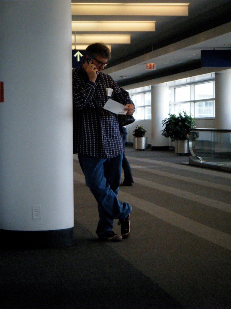 Photo of Parker on the phone leaning against a column at an international airport