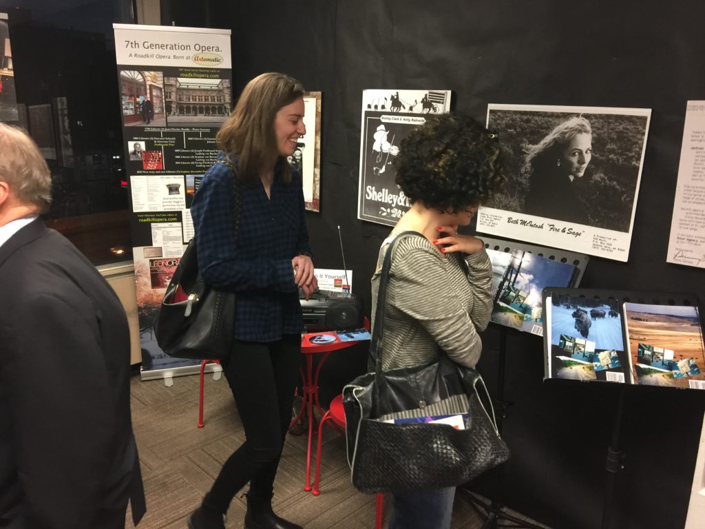 Photo of two women laughing while looking at A Roadkill Opera's set and sheet music