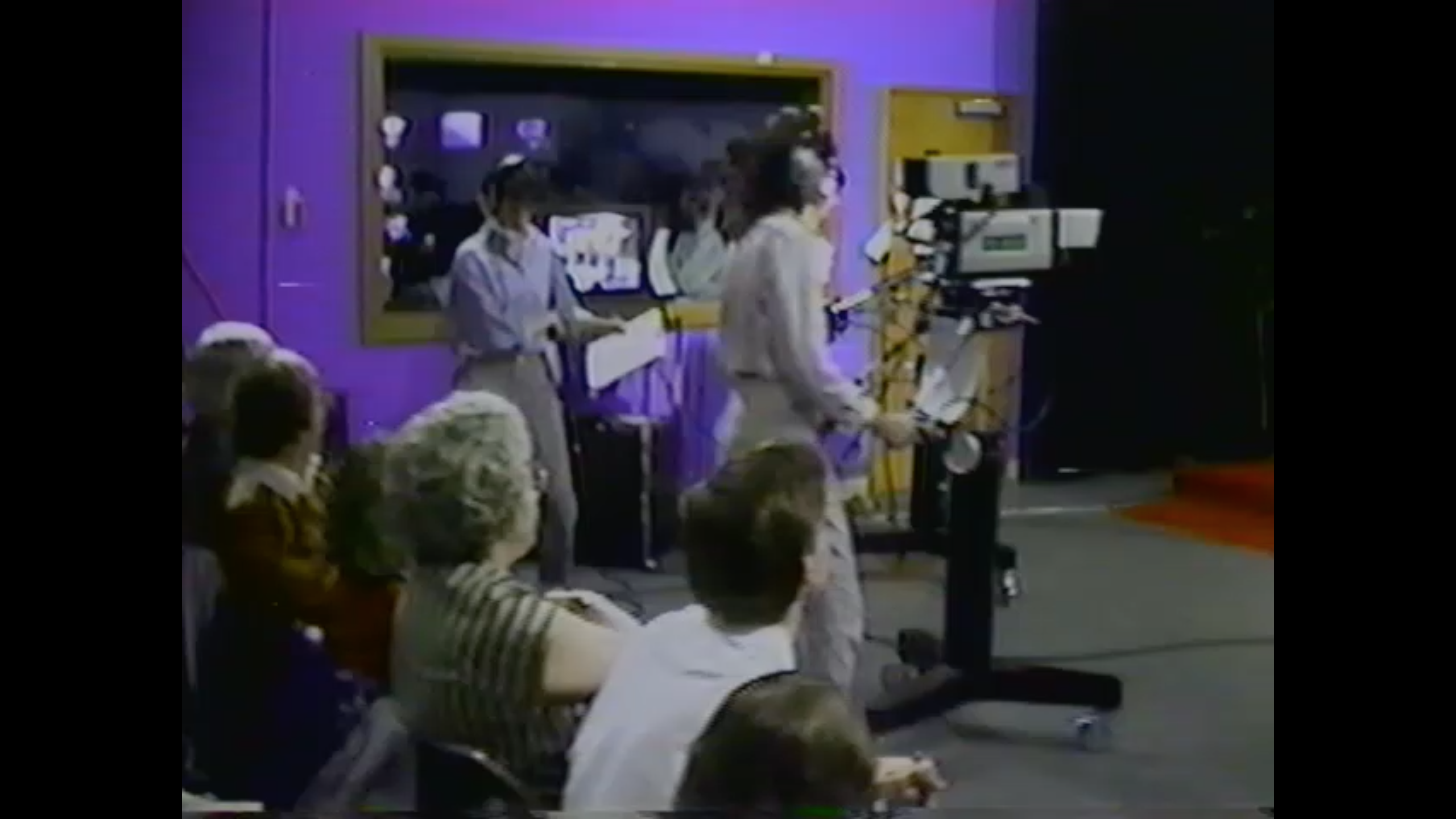 A view across the audience at The Friday Club in 1980s Evanston, Illinois. You can clearly see one camera operator (a second is behind that one), the floor manager, and the control room for this local sketch comedy/music live broadcast.