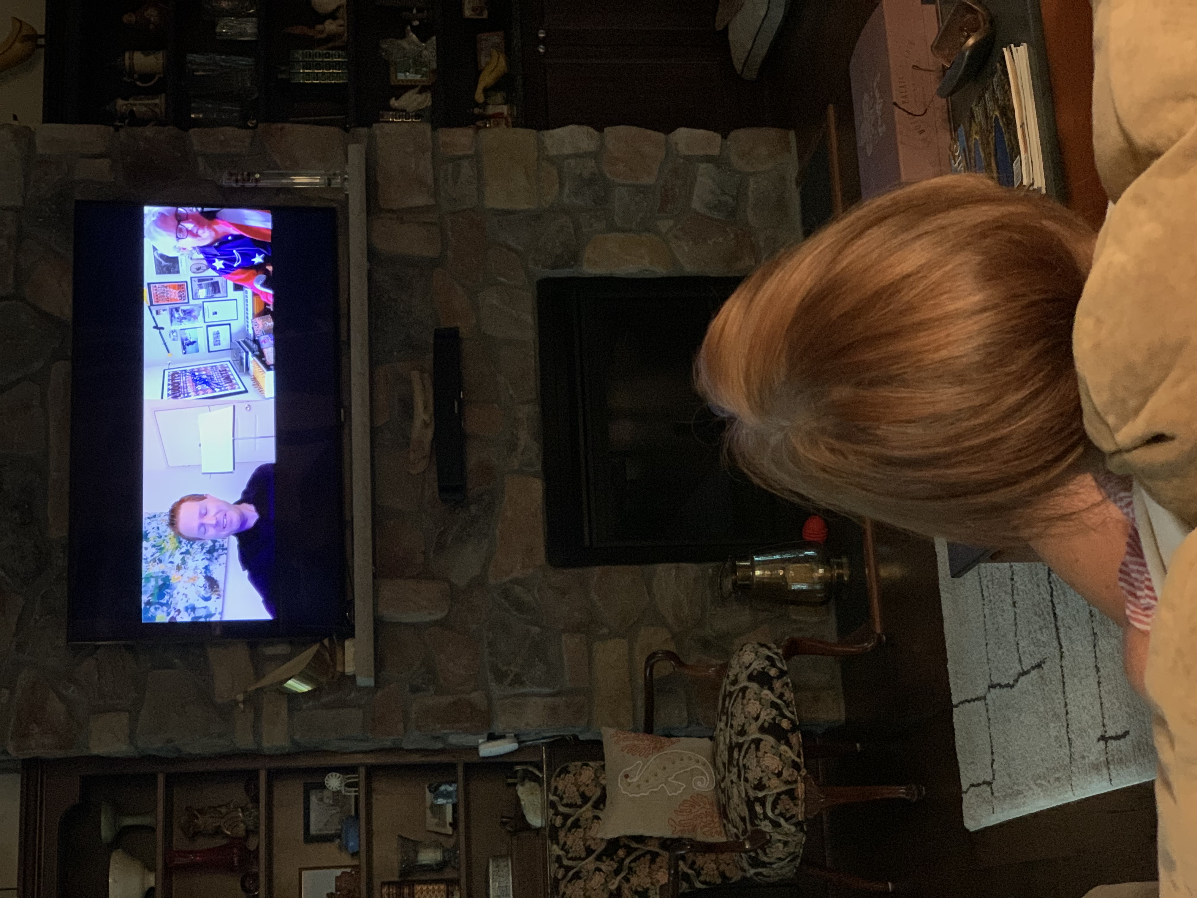 Photo of woman watching the livestream on a television set above a fireplace.